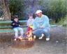 The boys cook hot dogs in the campfire